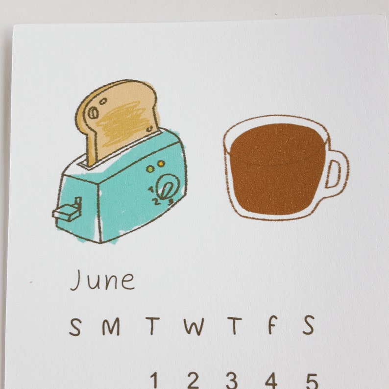 May include: A calendar page for June with a cartoon illustration of a toaster with a slice of bread popping up and a cup of coffee. The days of the week are labeled S M T W T F S and the numbers 1 2 3 4 5 are visible.