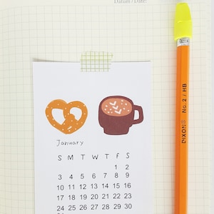 May include: A January calendar with a pretzel and a cup of hot chocolate illustration. The calendar shows the days of the week and the numbers 1 through 30.