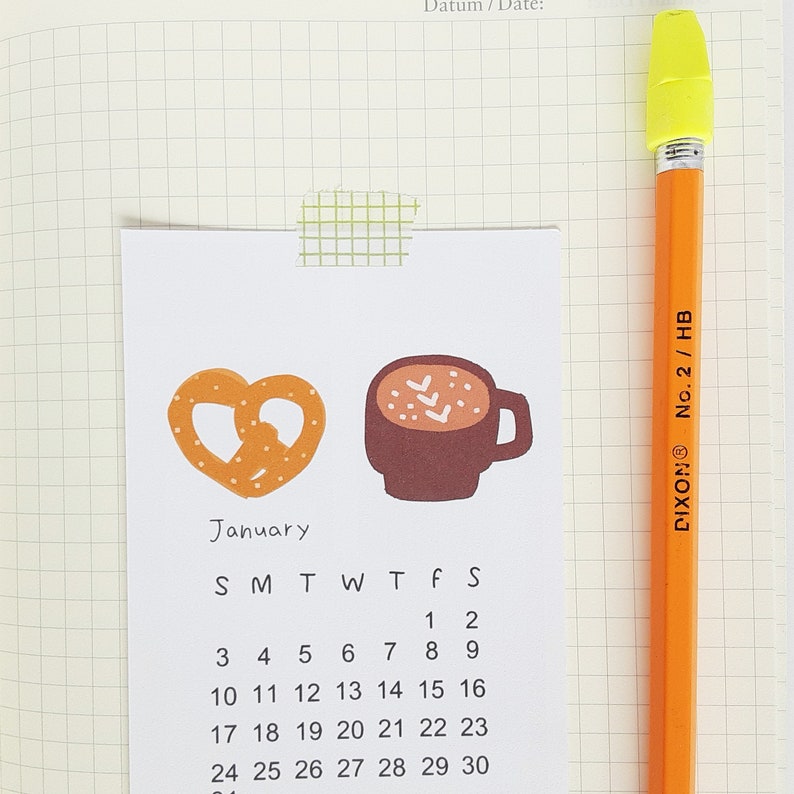 May include: A January calendar with a pretzel and a cup of hot chocolate illustration. The calendar shows the days of the week and the numbers 1 through 30.
