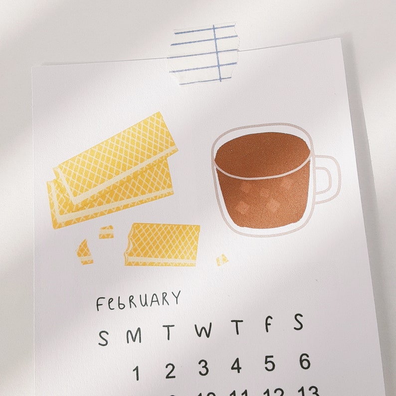 May include: A February calendar with a cup of coffee and a stack of waffle cookies. The calendar has the days of the week labeled S, M, T, W, T, F, S. The numbers 1, 2, 3, 4, 5, and 6 are visible on the calendar.