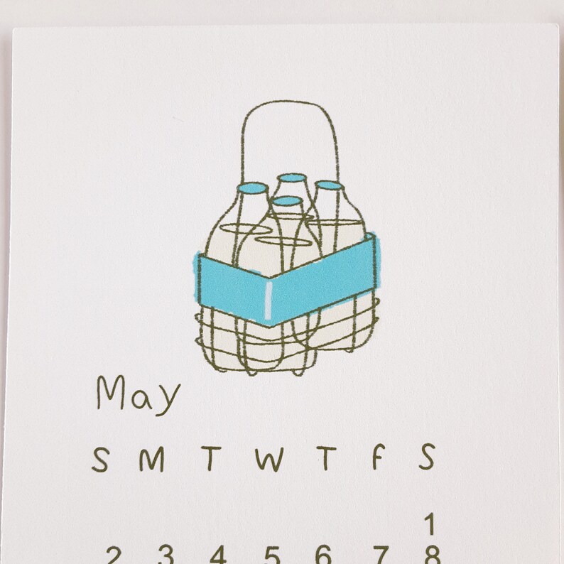 May include: A calendar for the month of May with a hand-drawn illustration of a milk crate with four milk bottles inside. The text "May" is written in brown below the illustration. The days of the week are abbreviated as "S M T W T F S" and the numbers 1 through 8 are written below the days of the week.