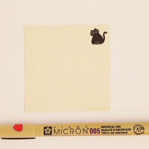 May include: A yellow sticky note with a black cat illustration and the text "Waverly Snow" printed on the bottom. A yellow pen with a red strawberry design and the text "Pigma Micron 005 Archival Ink Qualite d'Archivage Tinta de Archive" is also in the image.
