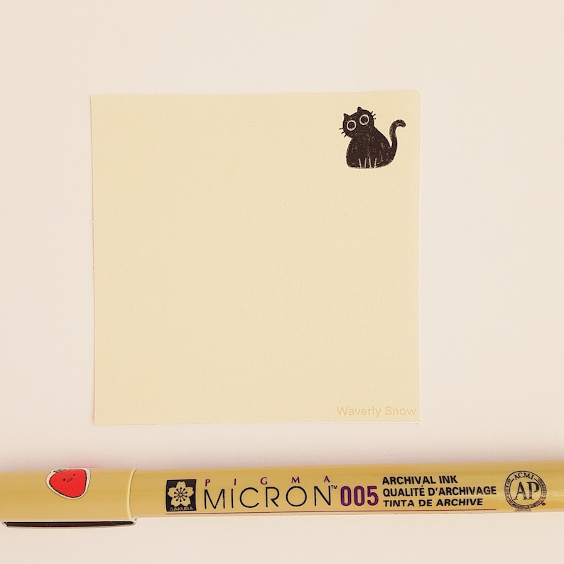 May include: A yellow sticky note with a black cat illustration and the text "Waverly Snow" printed on the bottom. A yellow pen with a red strawberry design and the text "Pigma Micron 005 Archival Ink Qualite d'Archivage Tinta de Archive" is also in the image.