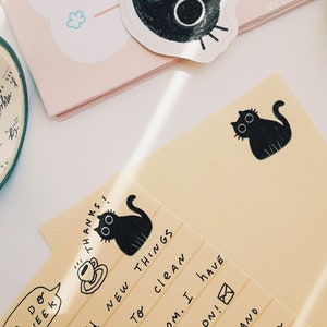 May include: A yellow notepad with black cat illustrations and handwritten text that reads "To Do WEEK", "THANKS", "add NEW THINGS", "To CLEAN", "ROOM. I HAVE", "SOON!", "AND", "TO".