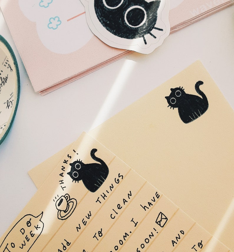 May include: A yellow notepad with black cat illustrations and handwritten text that reads "To Do WEEK", "THANKS", "add NEW THINGS", "To CLEAN", "ROOM. I HAVE", "SOON!", "AND", "TO".