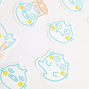 May include: Five blue and yellow cartoon cat stickers on a white background. The cats have different expressions and are outlined in blue.