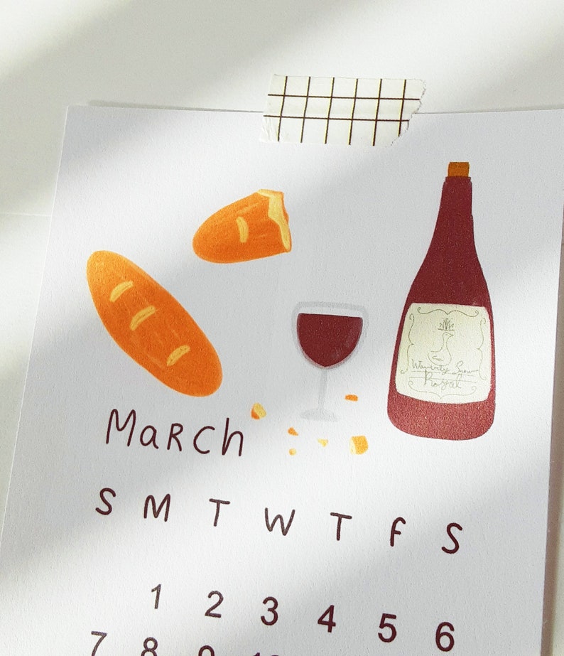 May include: A calendar page for March with a handwritten title and a simple illustration of a bottle of wine, a glass of wine, two loaves of bread, and a few scattered crumbs. The numbers 1 through 6 are visible on the calendar grid.