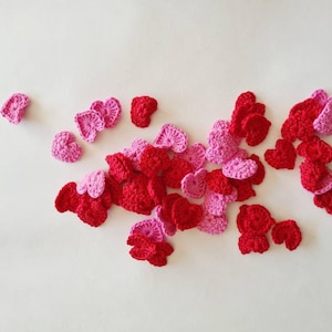May include: A collection of crocheted hearts in shades of pink and red. The hearts are scattered on a white background.