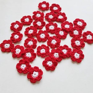 May include: A collection of red and white crocheted flowers. The flowers are small and delicate, with a white center and red petals.