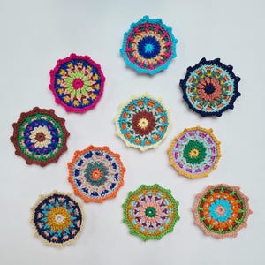 May include: Ten circular crochet coasters featuring intricate, multi-colored mandala patterns. Each piece displays a unique combination of vibrant yarn colors, including shades of blue, pink, orange, green, yellow, and brown, arranged in concentric, textured geometric designs.