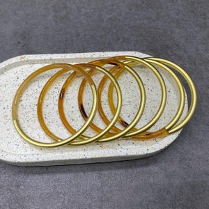 Op de afbeelding: Een set van zes gouden en bruine armbanden. De armbanden zijn op elkaar gestapeld en hebben een glanzende afwerking.