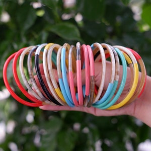 Könnte beinhalten: Ein Stapel bunter Hornarmbänder in verschiedenen leuchtenden Farben, darunter Rot, Gelb, Blau, Grün und Pink.