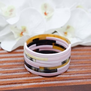May include: A stack of colorful bangles made of horn and resin. The bangles are pink, black, white, and yellow.
