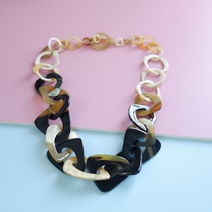 以下が含まれることがあります： 黒、茶色、クリームの角のつながったパーツでできた、ずっしりとした存在感のあるネックレスです。