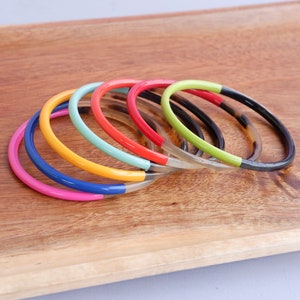 Op de afbeelding: Een set kleurrijke armbanden met een schildpadmotief. De armbanden zijn op elkaar gestapeld en gemaakt van hard plastic. De kleuren van de armbanden zijn roze, blauw, geel, groen en rood.