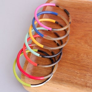 Könnte beinhalten: Ein Stapel bunter Armbänder mit einem schwarzen und weißen Hornmuster. Die Armbänder sind in einem Regenbogenmuster angeordnet, mit den Farben Grün, Rot, Blau, Gelb, Pink und Hellblau.