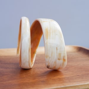 Op de afbeelding: Een witte en oranje schelpenarmband met een spiraalvormig ontwerp. De armband is gemaakt van natuurlijke materialen en heeft een unieke, organische uitstraling.