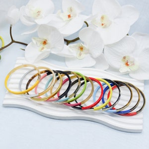 May include: A set of 12 colourful bangles with a natural horn base. Each bangle is half horn and half a bright colour, including yellow, red, blue, green, and pink.