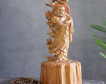 May include: A wooden sculpture of a deity with a long beard, wearing a robe and holding a scroll. The sculpture is standing on a wooden base.