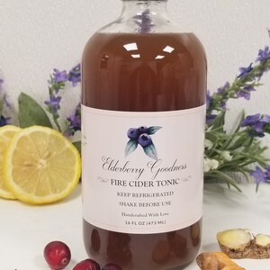 May include: A glass bottle of Elderberry Goodness Fire Cider Tonic. The bottle is brown and has a white label with the product name and instructions to keep refrigerated and shake before use. The bottle is 16 fluid ounces (473 ml).