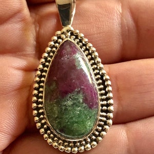 May include: A silver pendant with a green and pink gemstone set in a beaded border.