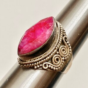 May include: A silver ring with a large, pink, faceted gemstone set in a decorative silver band.