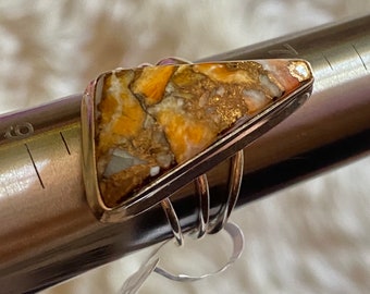 May include: A silver ring with a triangular shaped gemstone. The gemstone is a mix of brown, gold, and white colors. The ring is on a silver measuring tape.