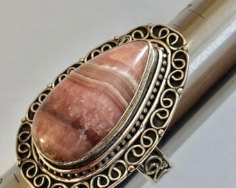 May include: A silver ring with a pink and white gemstone set in a decorative filigree design.