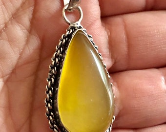 May include: A silver pendant with a yellow teardrop-shaped gemstone set in a silver ornate frame. The pendant is on a silver chain.