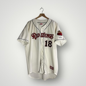 May include: Cream-colored baseball jersey with the words "Red Wings" in red script and the number "18" in black. The jersey has black trim and a logo on the sleeve. The jersey is hanging on a wooden hanger.