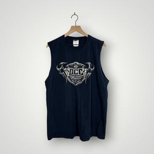 May include: Navy blue sleeveless t-shirt with a graphic design in silver and white. The graphic includes the letters "OCC" and the words "Orange County Choppers". The shirt is hanging on a wooden hanger.