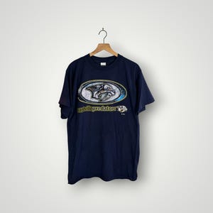 May include: Navy blue t-shirt featuring the Nashville Predators logo in a silver, white, and gold oval design. The text "nashvillepredators" is below the logo. The shirt is hanging on a wooden hanger.