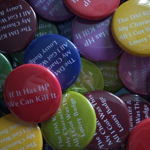 Puede incluir: Primer plano de un montón de botones redondos de colores con varias frases impresas en ellos. Las frases incluyen "The DM Killed All My Characters", "If It Has HP We Can Kill It", y "Lousy Badge All I Got Was This".