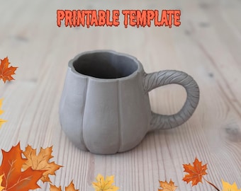 May include: A gray ceramic mug shaped like a pumpkin with a textured handle. The mug has vertical ridges and the words "PRINTABLE TEMPLATE" in orange text. Autumn leaves are scattered around the mug on a light wood surface.