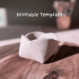 May include: A white concrete flower pot shaped like a folded paper flower. The pot is sitting on a wooden surface.