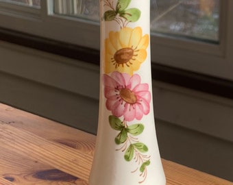 May include: A white ceramic vase with a yellow and pink floral design. The vase has a flared base and a narrow neck.