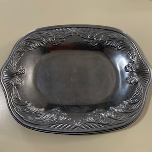 May include: A silver oval serving dish with an ornate design of leaves and flowers around the rim.