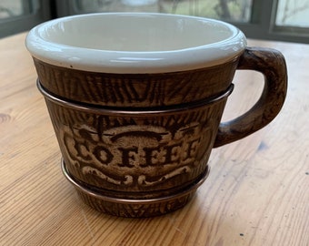 May include: A brown ceramic coffee mug with a white interior and a wood-grain design. The mug has a metal band around the top and bottom and the word "COFFEE" is embossed on the side.