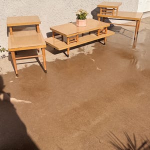 May include: Three mid-century modern style end tables with a light wood finish and brass accents. The tables are arranged in a row on a concrete patio.