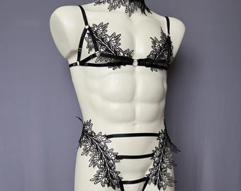May include: Black lace lingerie set on a white mannequin. The set includes a choker, a bra with straps, and a matching bottom. The lace features a floral design. The mannequin is displayed against a gray background.