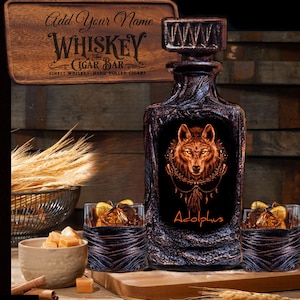 May include: A wooden whiskey decanter with a wolf design and the name "Adolphus" engraved on it. Two matching glasses with leather wraps are also included. The decanter and glasses are on a wooden surface with a sign that reads "Add Your Name Whiskey The Cigar Bar Finest Whiskey Hand-Rolled Cigars".