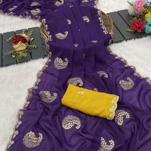 Puede incluir: Un sari morado vibrante con intrincados bordados dorados y una blusa amarilla a juego. El sari presenta un delicado estampado de cachemira y un borde festoneado. La tela parece ligera y fluida, perfecta para ocasiones especiales.
