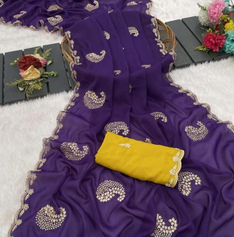 Puede incluir: Un sari morado vibrante con intrincados bordados dorados y una blusa amarilla a juego. El sari presenta un delicado estampado de cachemira y un borde festoneado. La tela parece ligera y fluida, perfecta para ocasiones especiales.
