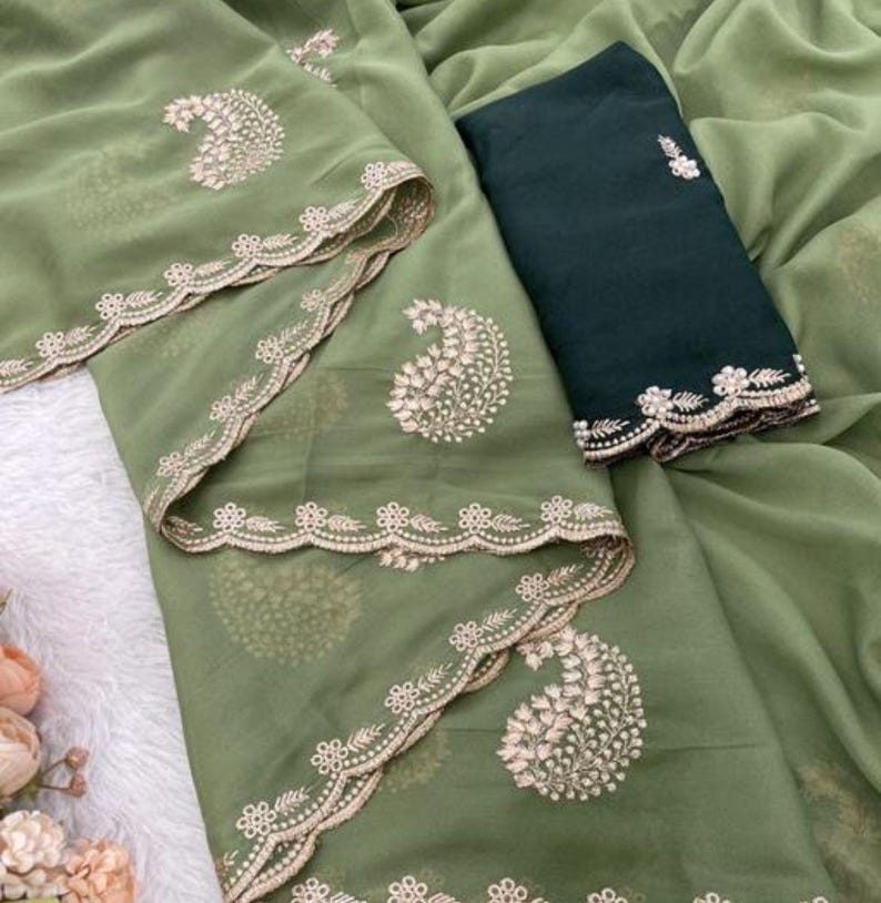 Puede incluir: Un conjunto verde oliva con bordados detallados. El conjunto incluye una parte superior y una parte inferior verde oscuro contrastante. La parte superior tiene un dise&ntilde;o de cachemira y un borde festoneado. La tela parece transparente y ligera, adecuada para climas c&aacute;lidos.