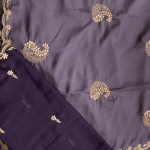 Puede incluir: Un conjunto de dos piezas con tela morada oscura y bordados dorados. La parte superior tiene un dise&ntilde;o de cachemira, y la pieza inferior peque&ntilde;os motivos florales. Los bordes de la parte superior est&aacute;n adornados con encaje dorado.