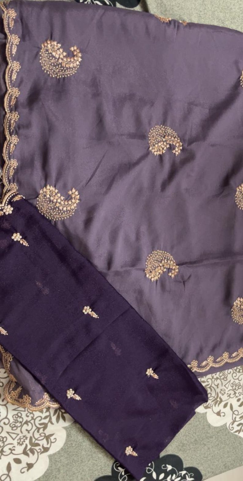 Puede incluir: Un conjunto de dos piezas con tela morada oscura y bordados dorados. La parte superior tiene un dise&ntilde;o de cachemira, y la pieza inferior peque&ntilde;os motivos florales. Los bordes de la parte superior est&aacute;n adornados con encaje dorado.