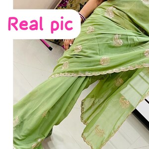 Puede incluir: Un sari verde claro con bordados dorados y un borde festoneado. El sari tiene intrincados detalles dorados y el texto "Real pic" en rosa.