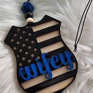 May include: Wooden car air freshener with a blue, white, and black American flag design. The word "wifey" is written in blue letters on the front. The back of the air freshener has the text "I've got your six."