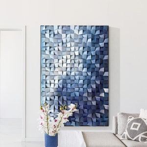May include: A white sectional sofa with a blue and white geometric wall art piece above it. A vase with white flowers sits on a white coffee table with a book and a decorative object.