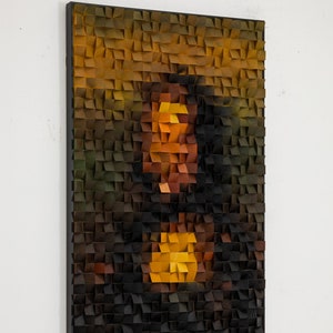May include: A wood mosaic artwork depicting a portrait of a person. The mosaic is made up of small, square pieces of wood in various shades of brown, orange, and yellow. The artwork is framed in black.